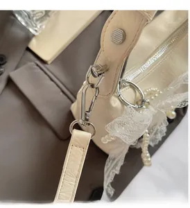 Détail d'un sac crème montrant les crochets argentés avec perles et nœud en dentelle blanche