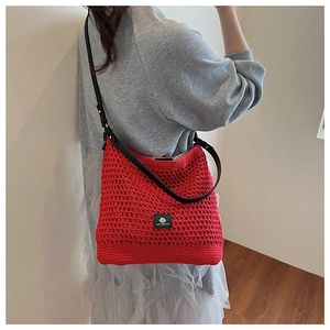 Détail d'un sac cabas en tricot ajouré rouge avec bandoulière en cuir noir et étiquette
