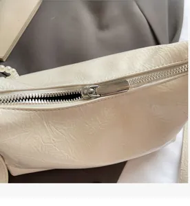 Détail de sac à main crème texturé avec fermeture éclair argentée et breloque perle