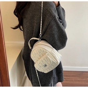 Detail of white quilted mini backpack with rhinestone decor and metal chain straps