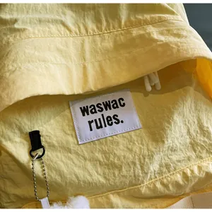 Close-up of yellow wrinkled fabric backpack with brand label and plush ball charm