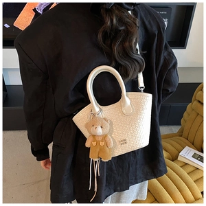 Détail d'un sac seau blanc à texture crocodile avec un charmant petit ours en peluche