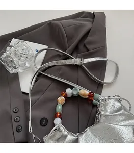 Detail of silver metallic bucket bag with colorful resin bead handle and pleated drawstring