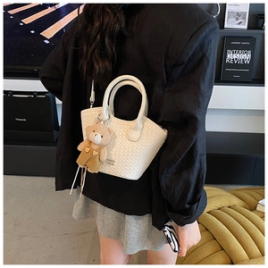 Détail du sac seau tressé blanc cassé avec poignées rondes et adorable pendentif d'ours