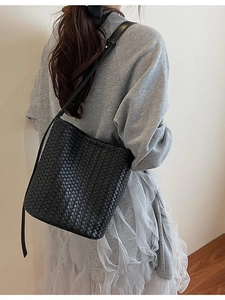 Sac seau minimaliste en cuir tressé noir avec bandoulière fine porté par un mannequin