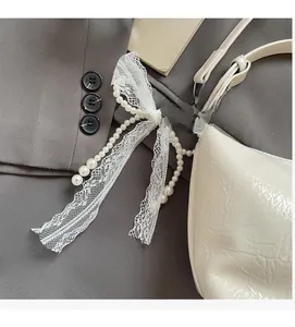 Détail d'un nœud en dentelle blanche et d'un charms en perles sur un sac crème