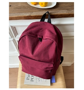 Detailed view of burgundy canvas backpack with front zipper pocket on a wooden stool