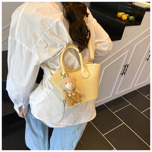 Détail du sac seau jaune tissé avec breloque d'ours en peluche porté en bandoulière