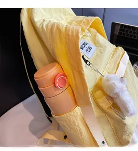 Detail of yellow backpack side pocket holding a water bottle and plush bear charm