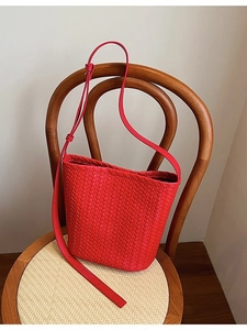 Sac seau tressé rouge avec bandoulière réglable sur un tabouret en bois dans un décor épuré