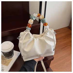Detailed texture of off-white pleated bucket bag with colorful beaded handle on steps