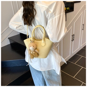 Détail du sac seau tressé beige avec breloque ours et bandoulière amovible