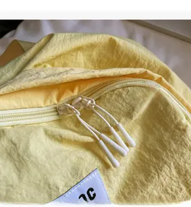 Detail of smooth double zippers with white cord pulls on a yellow nylon backpack