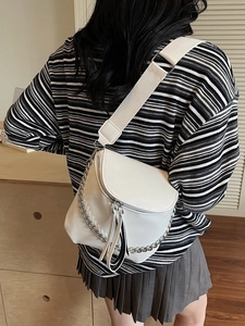 Fashionable white saddle crossbody bag with metal chain and wide fabric strap shown on model