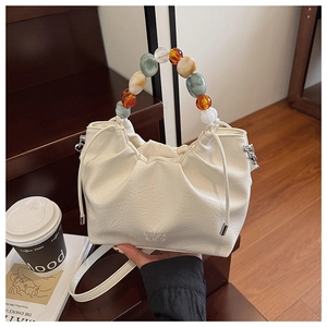 Detail of cream pleated bucket bag featuring colorful beaded handle and drawstring closure