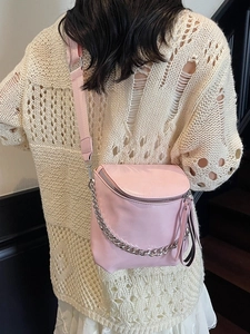 Pink saddle bag with metal chain and wide strap worn by a model in casual setting