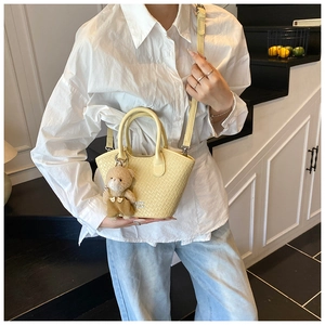 Détail du sac seau tissé jaune pâle avec charm ourson et double poignée supérieure
