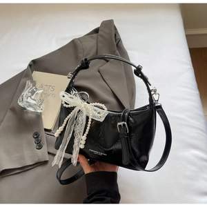 Détail du sac à main en cuir verni noir avec nœud en dentelle blanche et perles