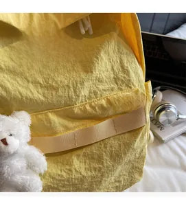 Detail of light yellow backpack with plush bear pendant and soft wrinkled fabric texture
