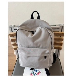 Detail view of a minimalist light grey canvas backpack with a spacious front zipper pocket