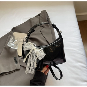 Détail d'un sac à main en cuir noir brillant avec nœud en dentelle et chaîne en perles