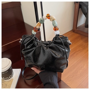 Detail of black pleated bucket bag with a colorful beaded handle on a wooden stair