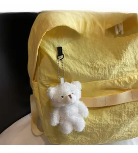 Detail of yellow nylon backpack featuring slogan label and a white plush bear charm