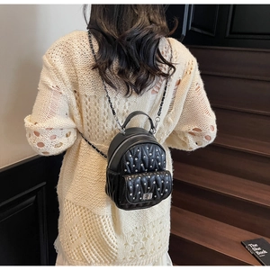 Detail of a mini quilted black leather backpack with silver studs and chain straps