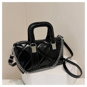 Detail view of black glossy quilted boston bag with silver chain and crossbody strap