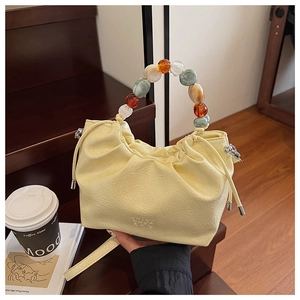 Detail of light yellow pleated bucket bag featuring colorful resin beaded handle and soft PU texture