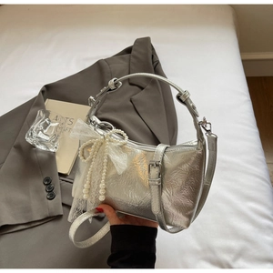 Détail d'un sac argenté plissé avec breloque décorative en perles et nœud en dentelle