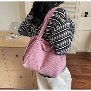 Detailed view of pink nylon tote bag with drawstring closure worn by a model in a cozy room
