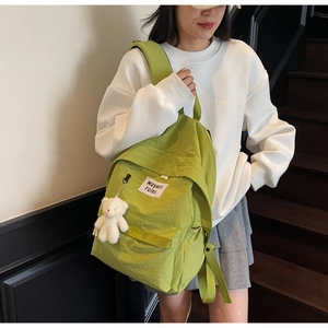 Dettaglio dello zaino verde chiaro con ciondolo a orsetto bianco e toppa con logo