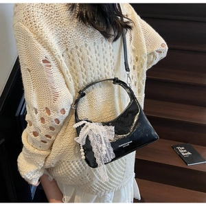 Détail du sac en cuir verni noir avec nœud en dentelle et pendentif perle sur escalier