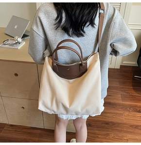Close-up of beige canvas tote with brown leather handles and embossed logo details