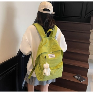 Dettaglio zaino in nylon verde lime con ciondolo a forma di orso e toppa logo sul retro