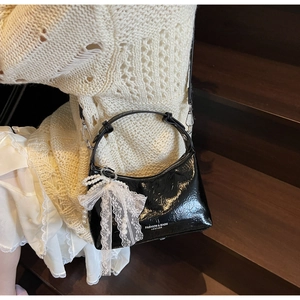 Détail du sac en cuir verni noir avec nœud en dentelle et pendentif en perles élégant