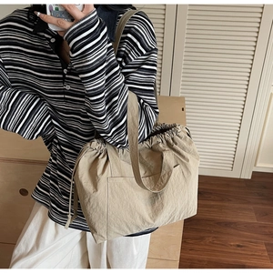 Detail of khaki nylon tote bag with drawstring closure and exterior pocket on a model