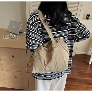 Back view of model wearing a khaki nylon tote bag with drawstring and large outer pocket