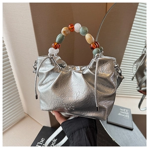 Detail of silver pleated bucket bag featuring a colorful beaded handle and metal texture