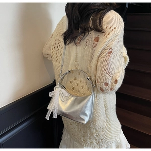 Détail du sac argenté texturé avec nœud en dentelle et breloques en perles