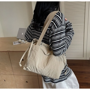 Detailed side view of large beige nylon tote bag with drawstring closure on model