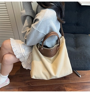 Close-up of a canvas tote bag with brown leather details worn by a model in a room
