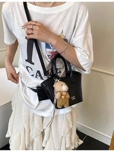 Sac seau tissé noir chic avec breloque ours et bandoulière réglable porté par un mannequin