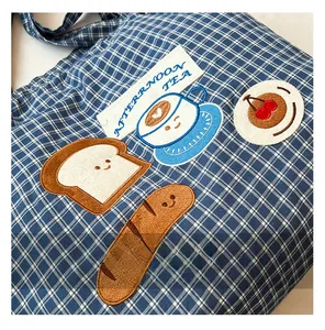 Detail of blue checkered canvas tote featuring breakfast themed embroidery and tea label
