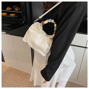Detail of white pleated bucket bag with amber resin bead handle and embossed logo