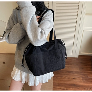 Close-up of black nylon drawstring tote bag worn by a model in a minimalist home setting