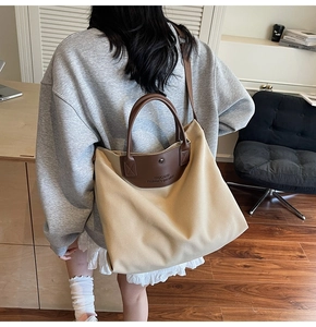 Detail of minimalist beige canvas tote bag with brown leather handles worn by model