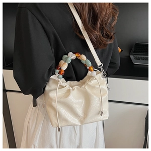 Detail of off-white pleated bucket bag with colorful beaded handle and drawstring closure