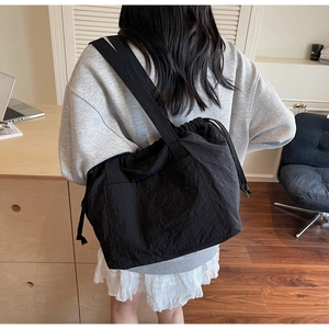Rear view of a model wearing a large black nylon tote bag with drawstring detailing